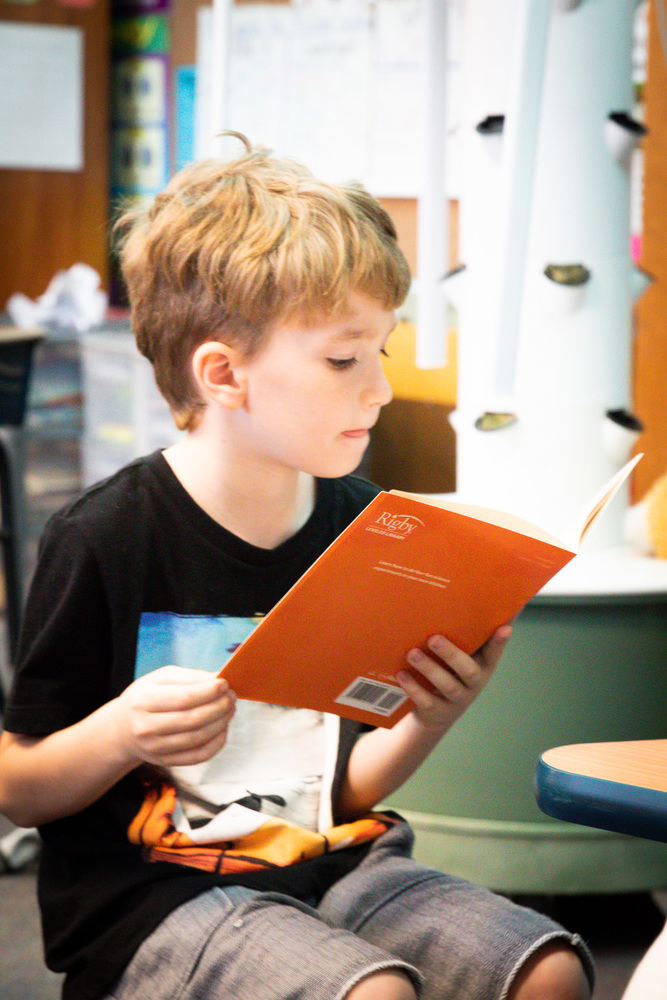 A boy reading a book with an orange cover