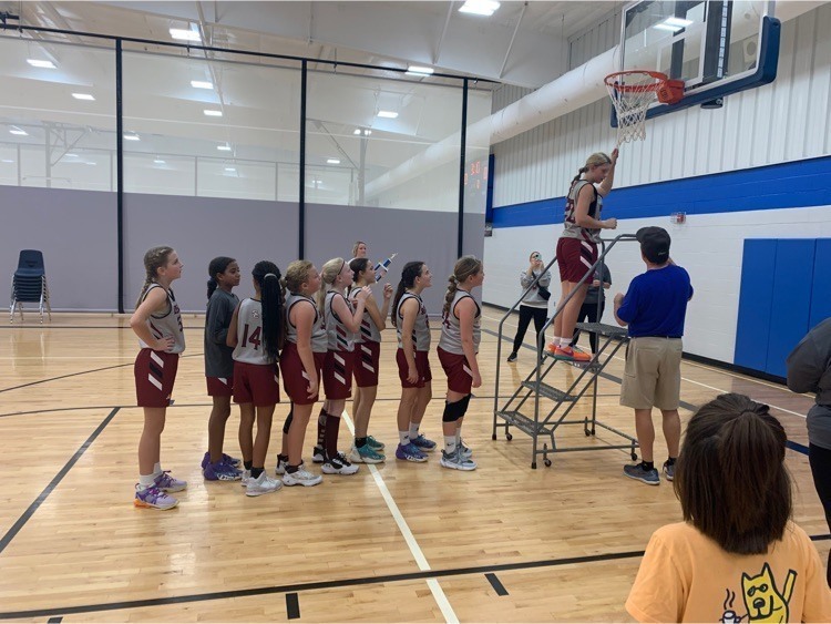 A line of girls in basketball jerseys waiting to cut a piece of the net down